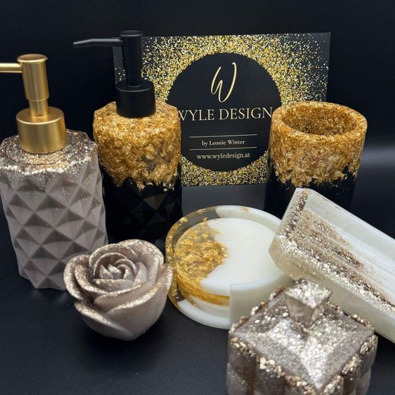 Eine Kollektion luxuriöser Badzubehör, darunter ein Seifenspender, eine Seifenbar, eine rosenförmige Seife und eine Kerze mit goldener Oberfläche auf einer schwarzen Oberfläche.