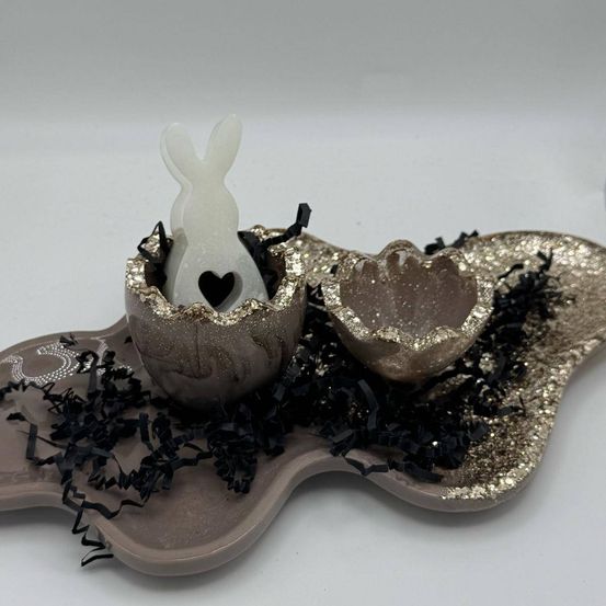Ein dekoratives Ei auf einem Tablett mit Glitzer und schwarzen Bändern, mit einer weißen Hasenfigur darin