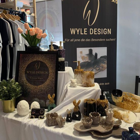Ein weißer Tisch mit verschiedenen Gegenständen darauf, einschließlich eines Schildes von Wyle Design mit einer Blumenarrangement im Hintergrund.
