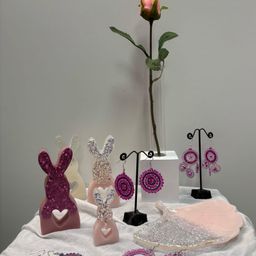 Ein Tisch mit verschiedenen rosa und glitzernden hasenförmigen Objekten, einem Teller und einer Rose in einer Vase.