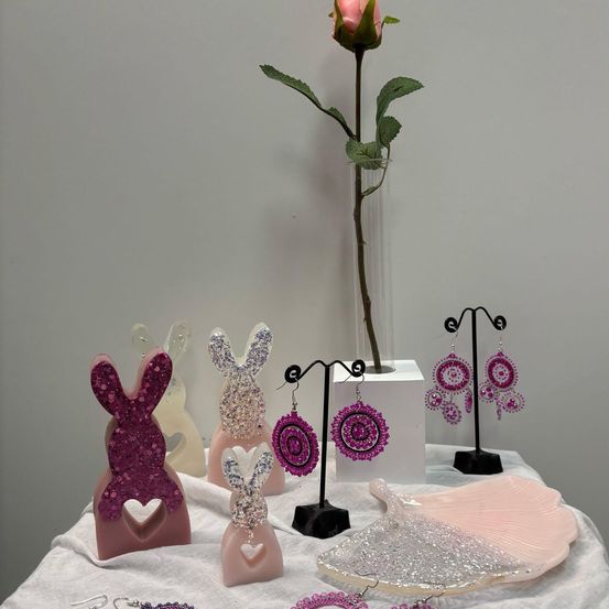 Ein Tisch mit verschiedenen rosa und glitzernden hasenförmigen Objekten, einem Teller und einer Rose in einer Vase.