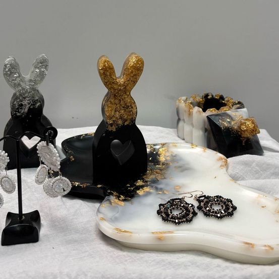 Eine Schmuck-Ausstellung zeigt zwei Hasenfiguren, eine in Gold und eine in Silber, auf einer weißen Marmorschale. Die Schale enthält ein Paar Perlenohrringe und eine Perlenkette.