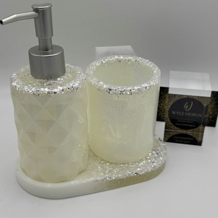 Ein Badezimmer-Set mit einem Seifenspender und einem Glasbecher auf einer weißen Marmorbasis. Das Set ist mit Silberglitter verziert.