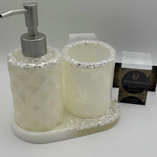 Ein Badezimmer-Set mit einem Seifenspender und einem Glasbecher auf einer weißen Marmorbasis. Das Set ist mit Silberglitter verziert.