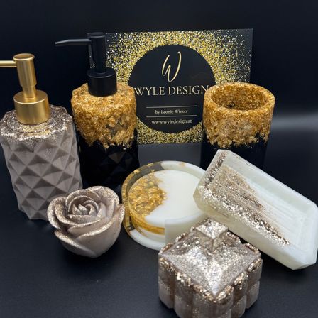 Eine Kollektion von Luxus-Seifenspendern und Seifen von Wyle Design mit schwarzen und goldenen Designs, einer rosenförmigen Seife und einer Visitenkarte im Hintergrund.