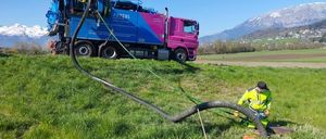 Ein Mann benutzt einen großen Schlauch, der mit einem blauen und rosa Truck verbunden ist, um Wasser in den Boden in einem Grasfeld zu pumpen.