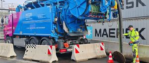 Ein blauer Recycling-LKW steht am Straßenrand, bedient von einem Mann in einem gelben Overall. Er hat einen großen, zylindrischen Tank auf dem Rücken.
