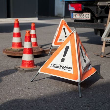 Ein Baustellenbereich mit Verkehrskegel und Warnschildern ist sichtbar und weist auf Kanalarbeiten hin. Ein Fahrzeug mit dem Kennzeichen FK 996 CJ ist in der Nähe geparkt.