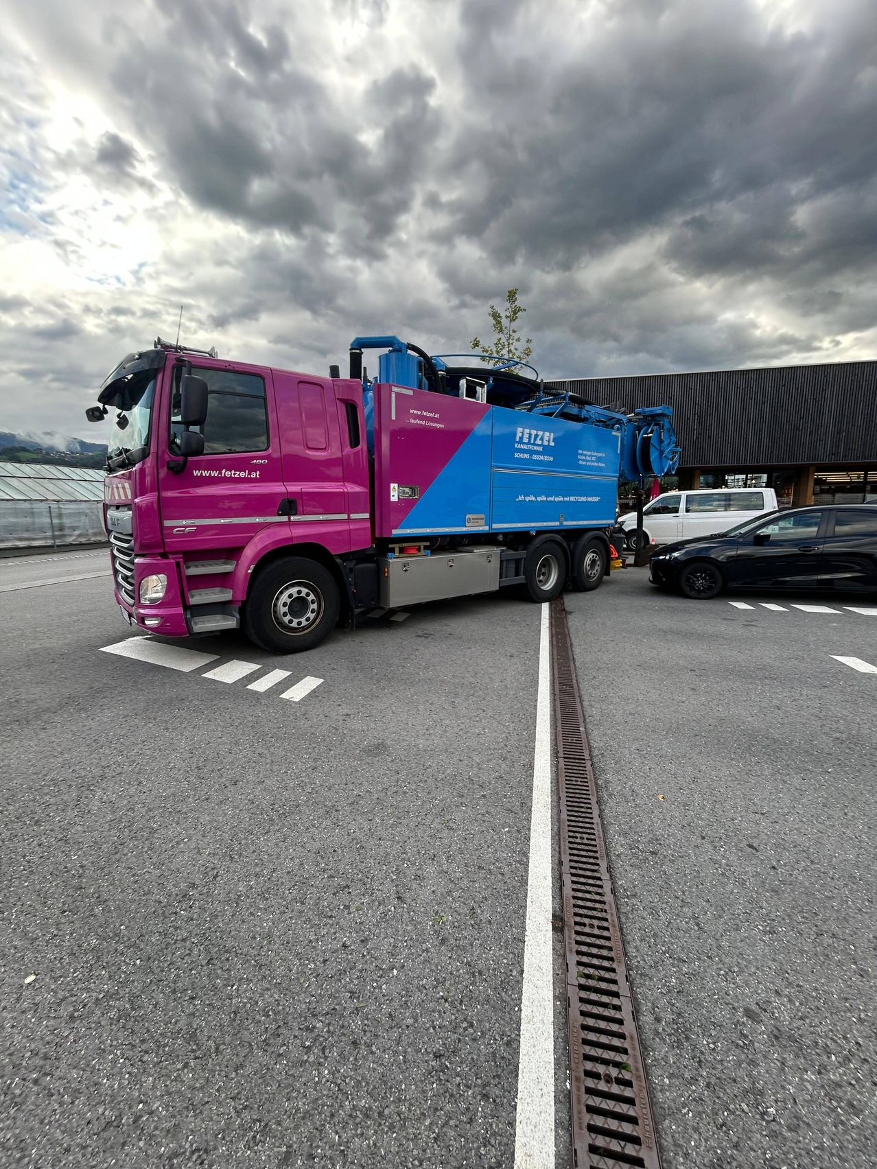 Ein pinker und blauer Lastwagen ist am Straßenrand geparkt, mit einem schwarzen Auto in der Nähe. Der Lastwagen hat das Wort 'FETZEL' an seiner Seite.