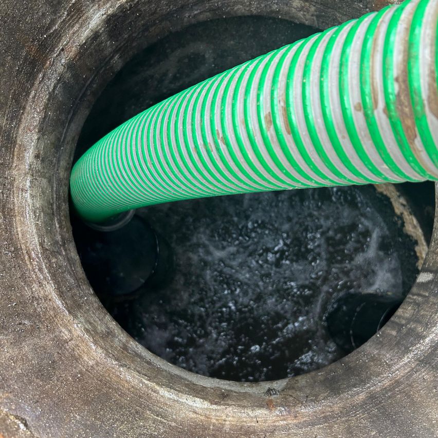 Ein grüner Schlauch ist in einen mit Wasser gefüllten Betonbrunnen eingeführt. Der Schlauch ist aufgewickelt und scheint zum Pumpen oder Reinigen verwendet zu werden.