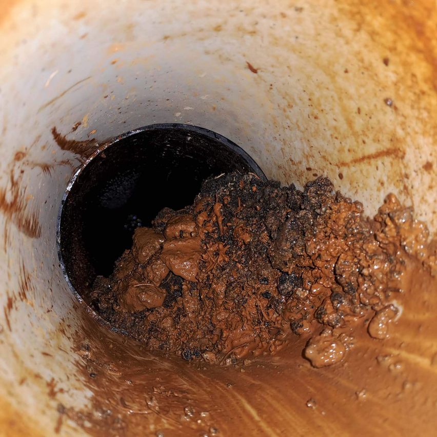 Eine Nahaufnahme eines verstopften Abflusses mit einer Mischung aus braunem Schlamm und Schmutz. Der Abfluss ist mit dickem, schlammigem Material gefüllt.
