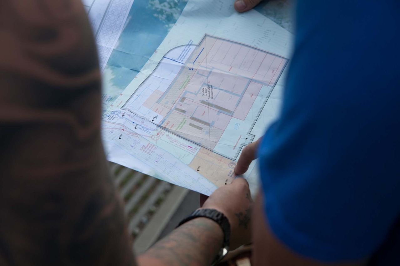 A person is holding a piece of paper with a map and diagrams, possibly a blueprint, on a wooden surface.