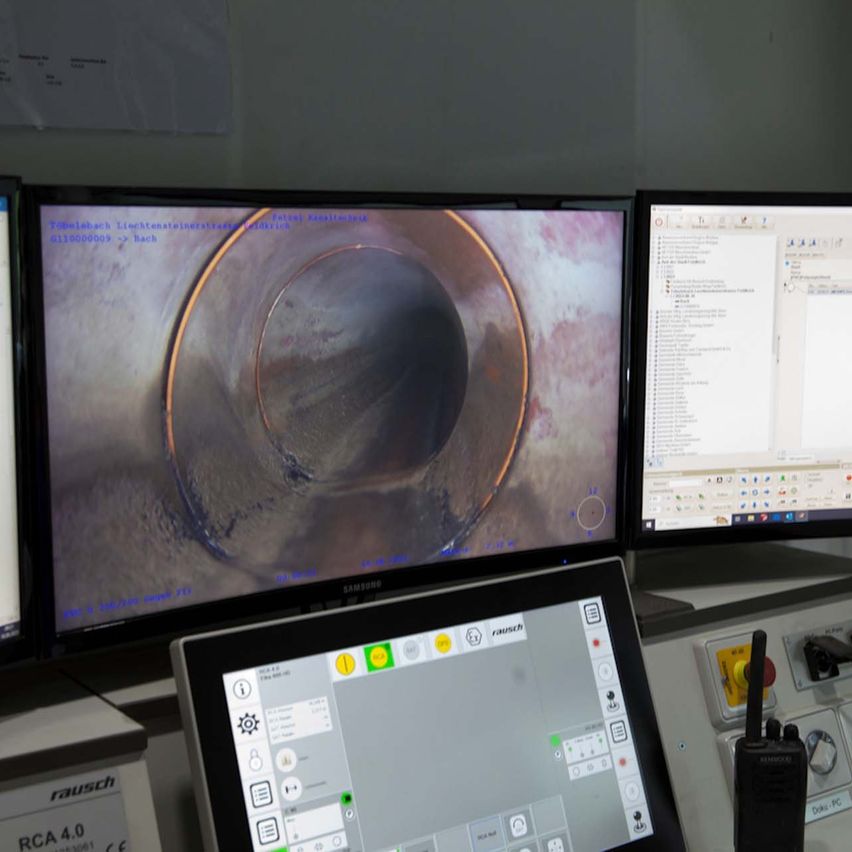A room with multiple computer monitors displaying a circular inspection image of a pipe and various computer applications.