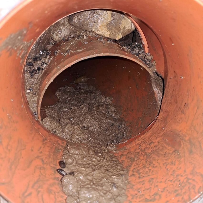 A clogged drainpipe with a mixture of sludge and debris. The inside of the pipe is dirty, with small stones and brownish-gray sediment.