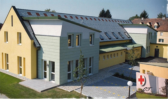 Eine Luftaufnahme eines gelben Gebäudes mit einem roten Kreuzschild davor.