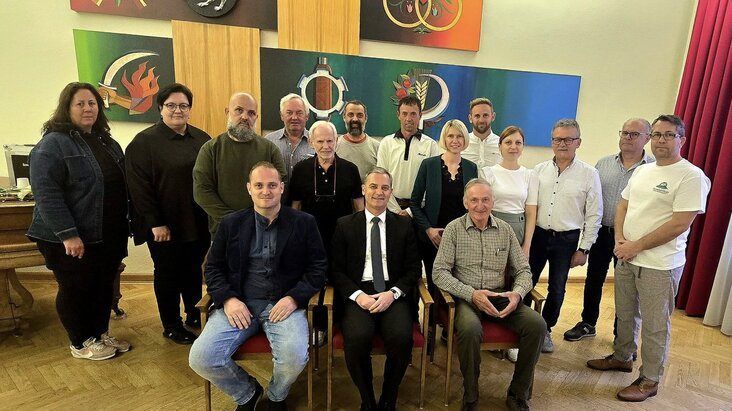 Eine Gruppe von Menschen in formeller und lässiger Kleidung posiert für ein Foto in einem Raum mit Holzböden und Gemälden an der Wand.