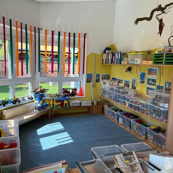 Ein Raum voller bunter Spielzeuge und organisierter Aufbewahrungsboxen, Regale mit Büchern und Bildern und eine bunte Fahne, die hängt.