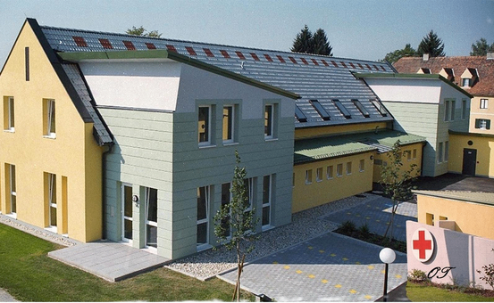 Ein gelbes und weißes Gebäude mit Solarmodulen auf dem Dach und einem roten Kreuz-Schild an der Wand.