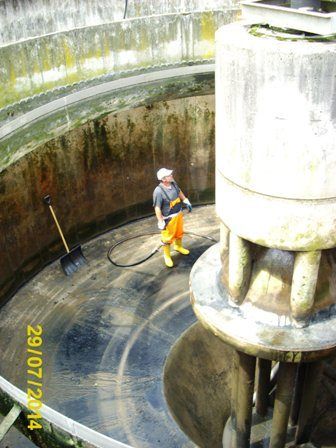 Ein Arbeiter in einem grauen Shirt und gelben Hosen reinigt eine große industrielle Pumpe. Die Pumpe ist groß und zylindrisch, mit einer Schaufel in der Nähe. Das Datum 29/07/2014 ist im Bild sichtbar.