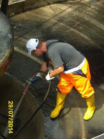 Ein Arbeiter in orangefarbener Hose und gelben Stiefeln reinigt einen großen Betontank mit einer Schlauch. Das Datum im Bild ist der 29. Juli 2014.