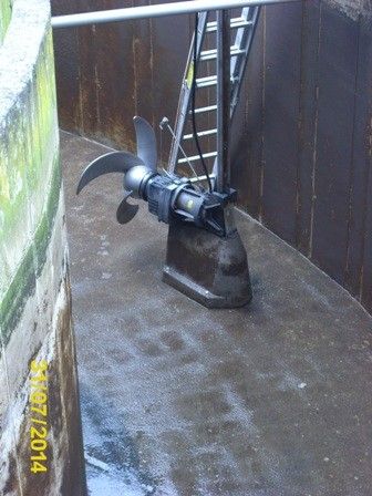 In einer industriellen Umgebung zeigt sich ein großer, rostiger Schiffspropeller, der an einer Betonwand befestigt ist. Dahinter befindet sich eine Leiter, und ein Datumsstempel vom 17.03.2014 ist links sichtbar.