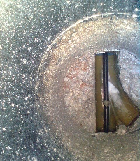 Eine Nahaufnahme einer kreisförmigen Öffnung in einem Betonboden zeigt einen Rohr, das durch die Öffnung führt. Das Rohr ist mit einem Riemen befestigt.