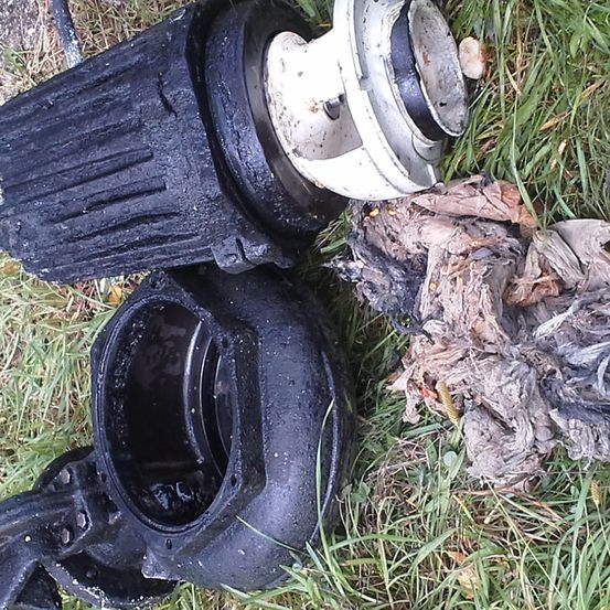 Ein schwarzes und weißes Maschinenteil, beschädigt und verbrannt, liegt auf Gras mit etwas Schutt.