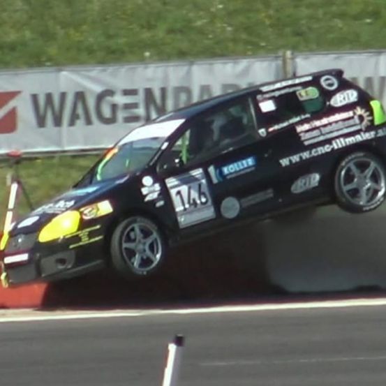 Ein schwarzer Rennwagen mit der Nummer 146 ist während eines Rennens auf einer Rennstrecke mit einer rot-weißen Barriere in der Luft.
