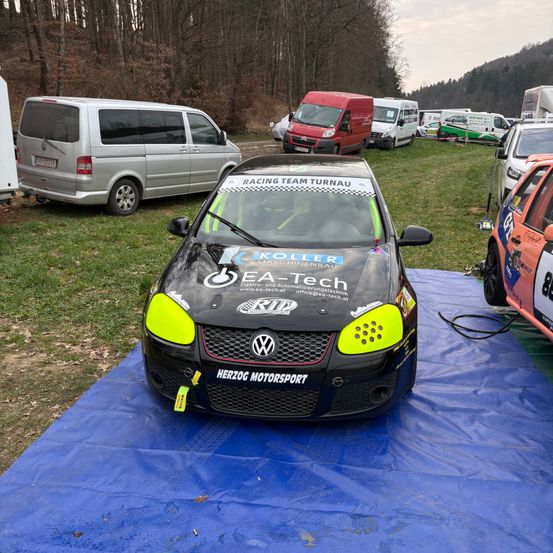 Ein schwarzer Rennwagen mit gelben und grünen Akzenten auf einer blauen Plane. Auf der Motorhaube steht EA-Tech.