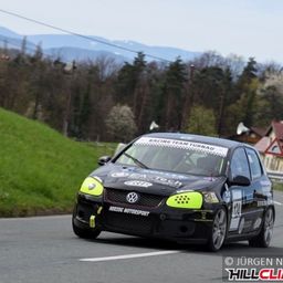 Ein schwarzer Volkswagen Polo GTI fährt auf einer kurvenreichen Straße. Das Auto hat ein Rennteam-Schild, gelbe Akzente und einen Berghintergrund.