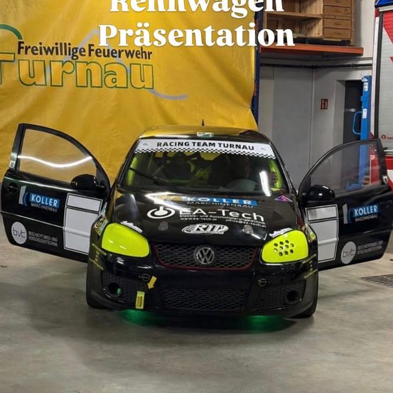Ein Rennwagen des Turnau Racing Teams steht mit offenen Türen in einer Garage. Das Auto ist schwarz mit gelben und grünen Akzenten. Der Banner liest 'Reinwagen Präsentation' in weiß.