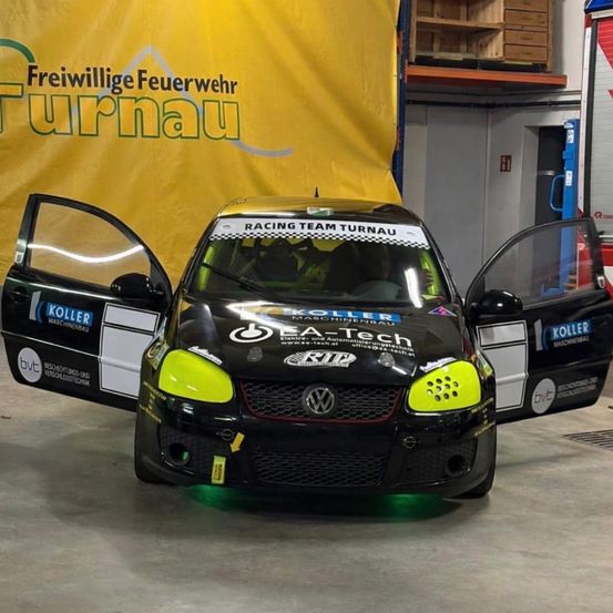 Ein schwarzer Volkswagen Golf GTI mit grünen Akzenten und geöffneten Türen, in einer Garage mit einem gelben Banner, das 'Freiwillige Feuerwehr Turnau' besagt.