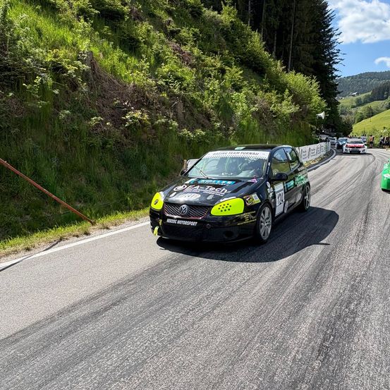Ein schwarzer und gelber Volkswagen Polo GTI fährt auf einer kurvenreichen Straße mit grünem Gras an der Seite. Andere Autos folgen dahinter.