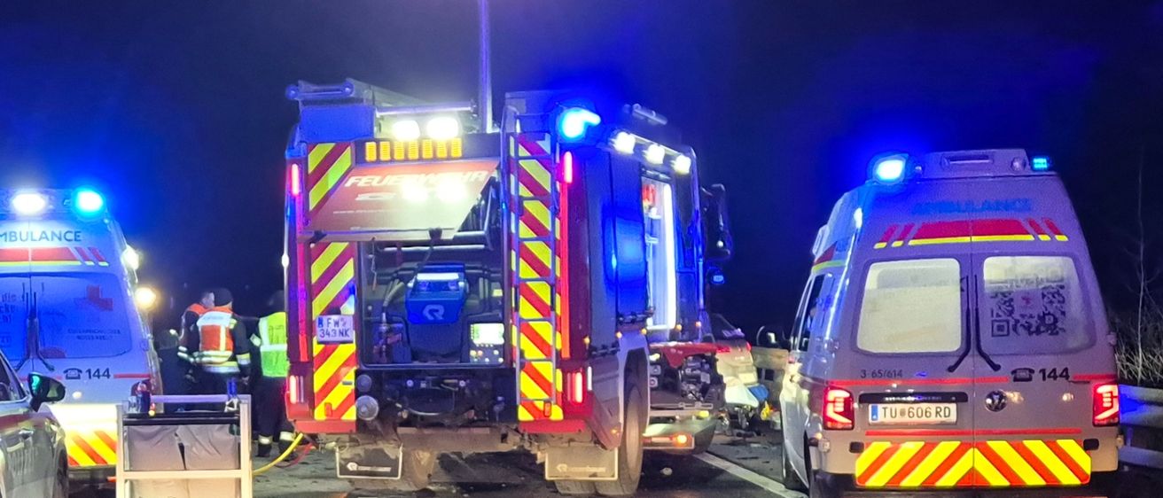 Rettungsfahrzeuge und Polizei sind am Unfallort eines Autounfalls auf einer Straße in der Nacht.