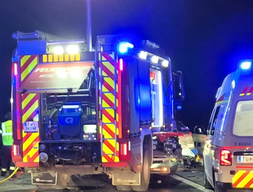 Rettungsfahrzeuge und Polizei sind am Unfallort eines Autounfalls auf einer Straße in der Nacht.