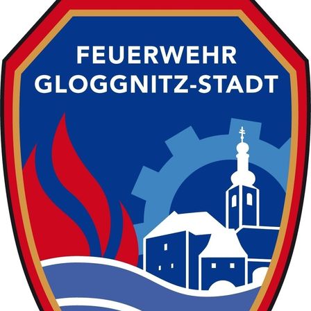 Ein blaues und rotes Emblem mit 'Feuerwehr Glognitz-Stadt' in Weiß geschrieben, darüber eine Darstellung einer Kirche, Gebäude und Flammen.