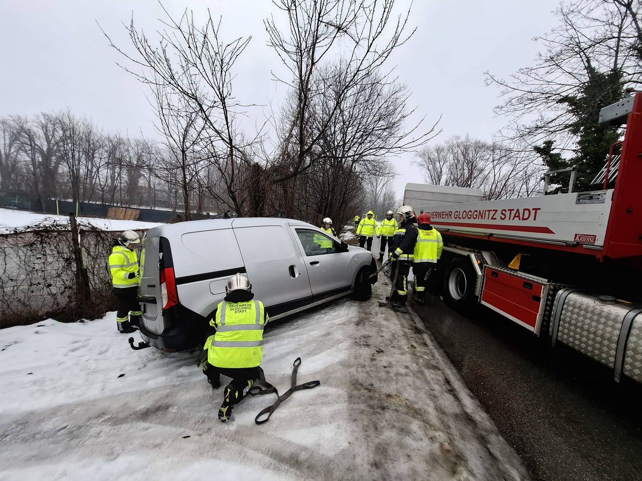 Feuerwehrleute in Warnwesten arbeiten an einem Fahrzeug unter verschneiten Bedingungen. Ein LKW ist neben ihnen geparkt.