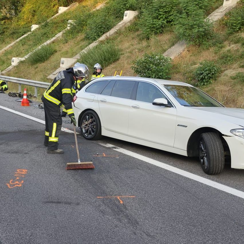 Feuerwehrmann reinigt Fahrbahn nach Unfall mit weißem Kombi auf Autobahn bei Graz