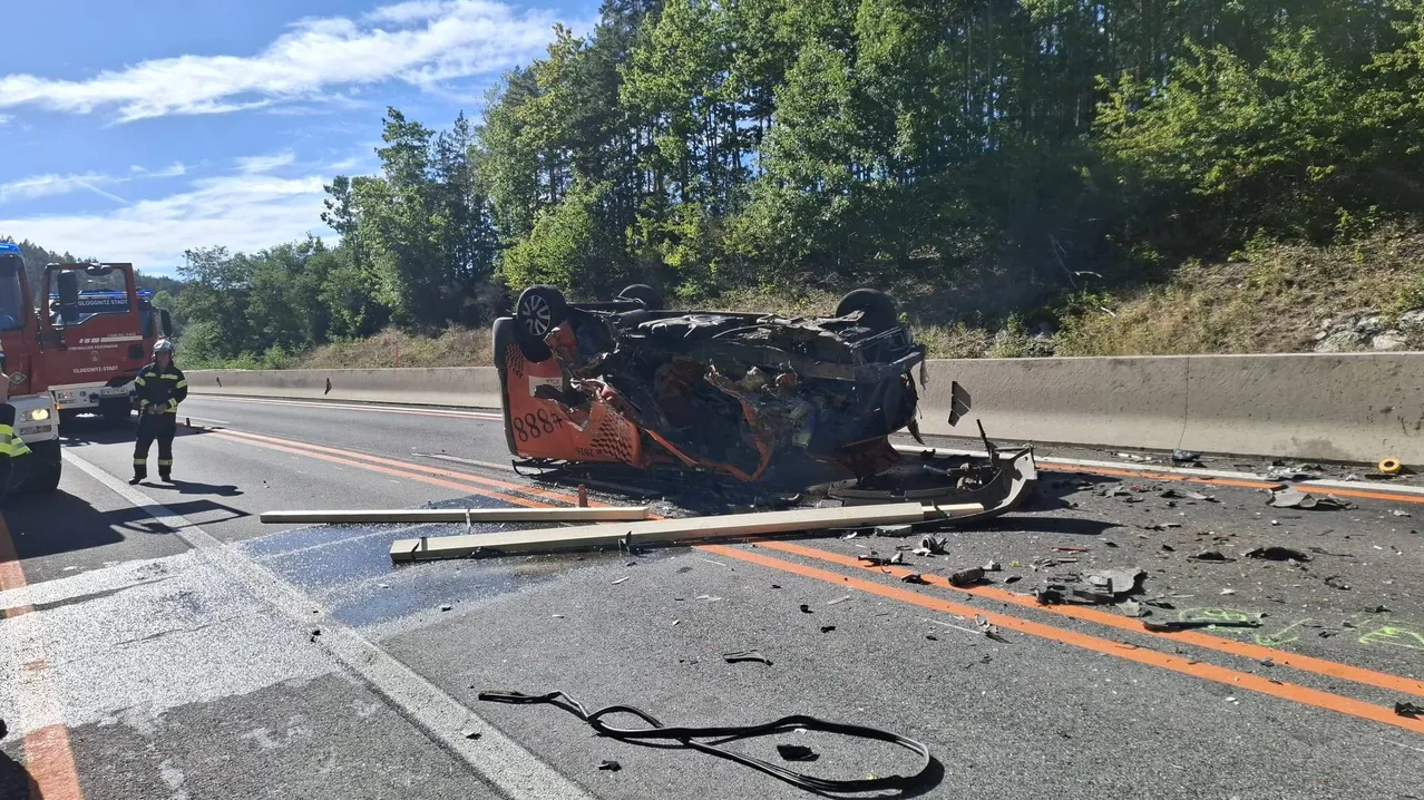 Ein umgestürztes Auto liegt an der Straßenseite, mit herumliegenden Trümmern. Das Auto hat die Nummer 888 auf seiner Seite.