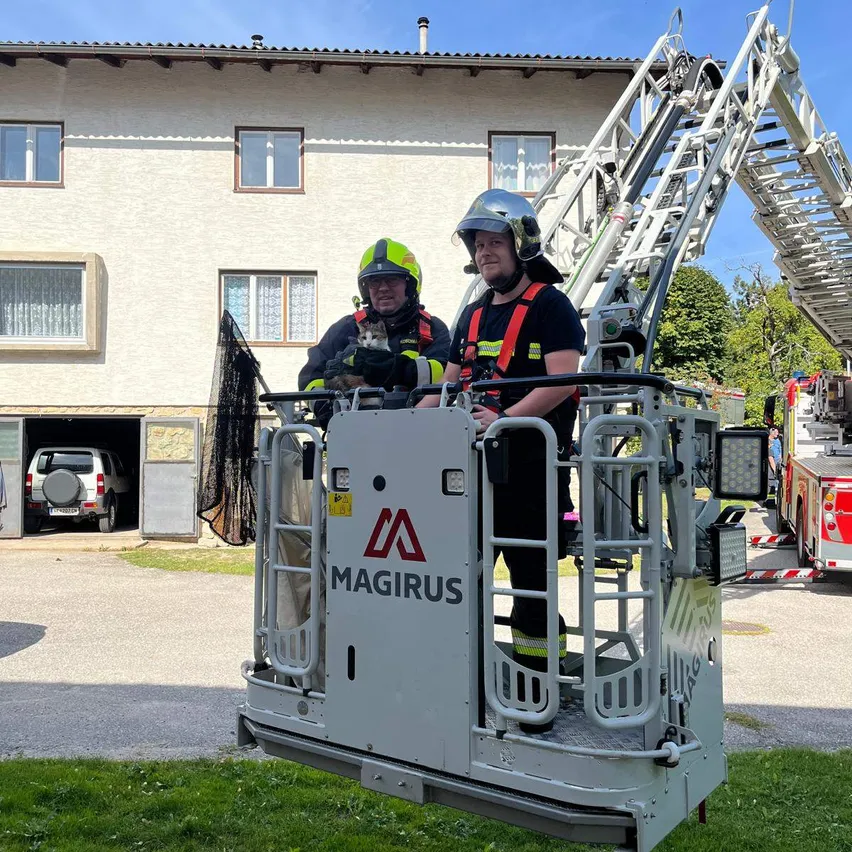 Zwei Feuerwehrleute stehen auf einer Leiter eines Feuerwehrwagens vor einem Haus.