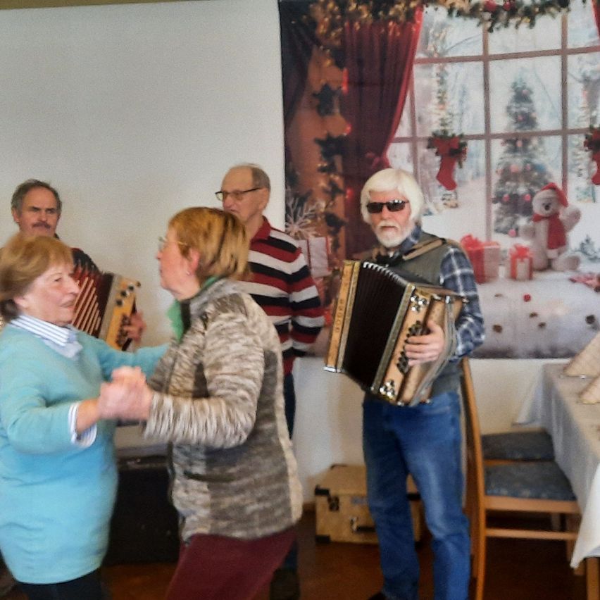 Gruppe von Menschen, die in einem Raum mit einem Weihnachtsthema an der Wand tanzen und Musikinstrumente spielen.