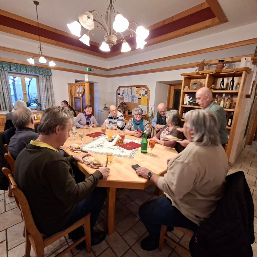 A group of elderly people sitting around a table with food and drinks. A chandelier hangs from the ceiling.
