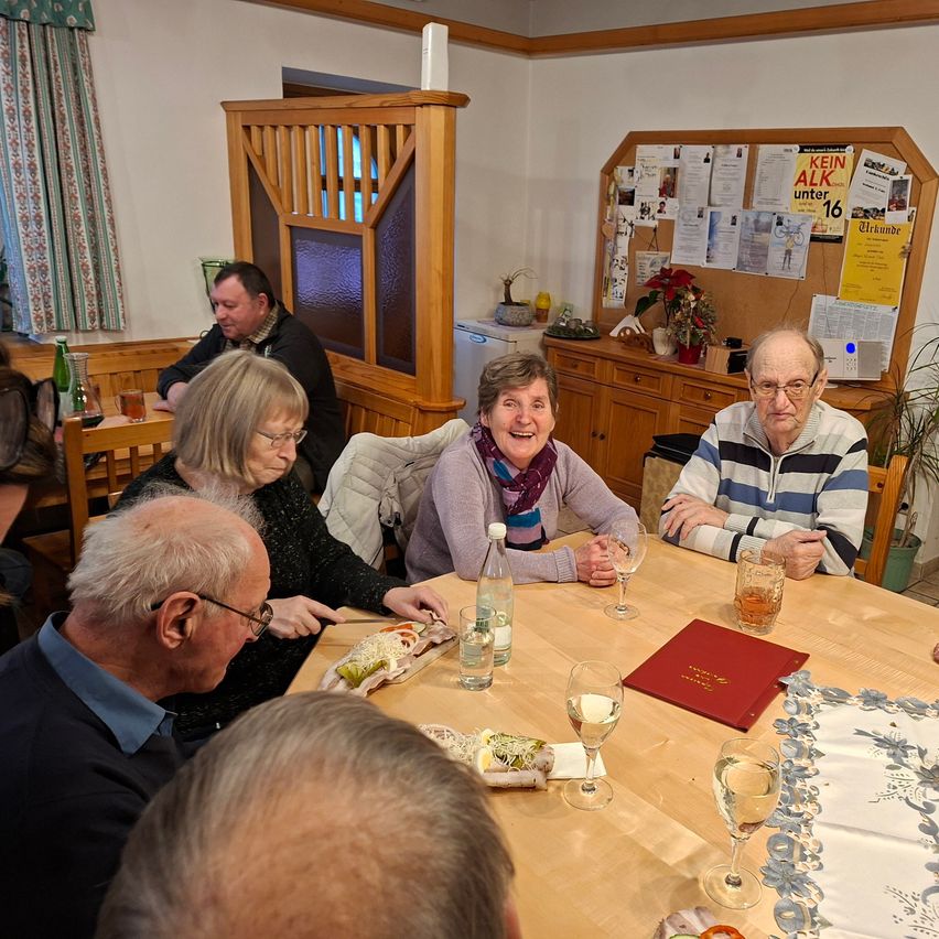A group of people are sitting around a table, having a meal. They are all smiling and appear to be enjoying themselves.