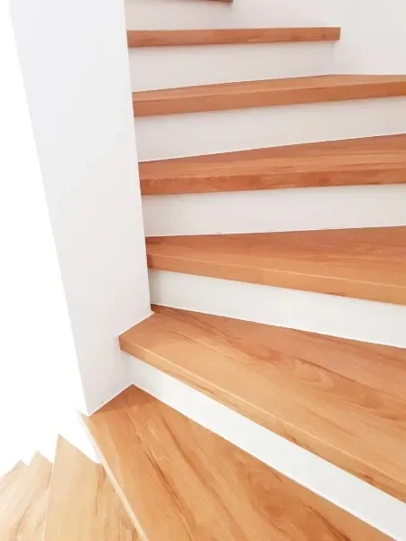 Eine Treppe aus Holz mit weißen Abschlüssen ist in einem Raum zu sehen. Die Treppe hat ein abgeschrägtes Design.
