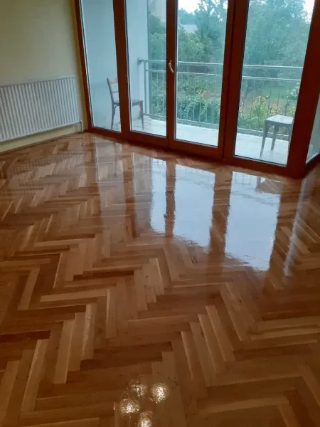 Ein Raum mit Holzboden und Glastüren, die zu einem Balkon mit Stühlen und einem Geländer führen, mit Blick auf einen Garten.