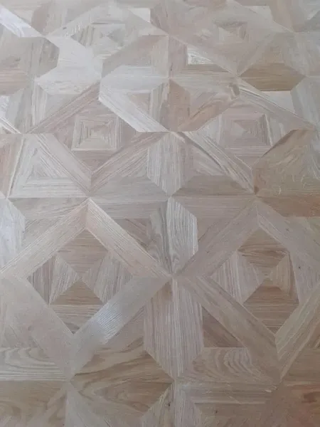 Eine Nahaufnahme eines hölzernen Parkettbodens mit einem geometrischen Muster aus sich kreuzenden Linien, die Diamanten und Quadrate bilden.