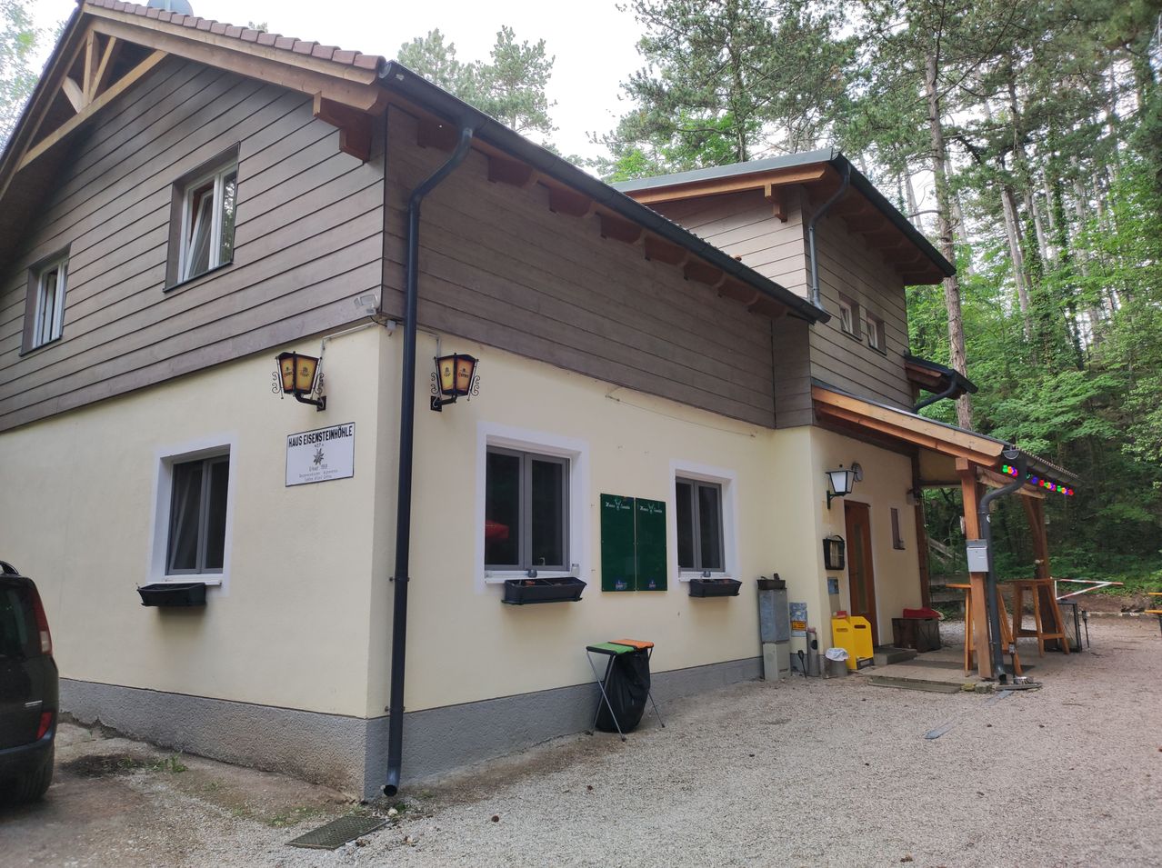 Ein zweistöckiges Gebäude mit beigefarbenen Wänden und einem braunen Dach. Es gibt drei Fenster im ersten Stock und drei im zweiten. Ein Mülleimer steht draußen.