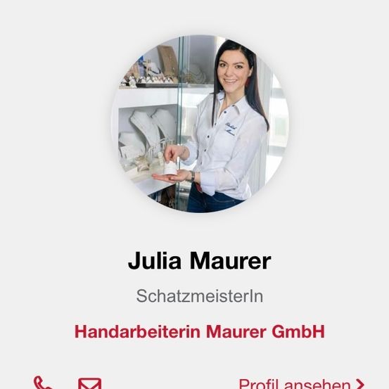 Eine Frau lächelt und hält ein Schmuckstück in der Hand. Der Text auf dem Bild lautet 'Julia Maurer, Schatzmeisterln, Handarbeiterin Maurer GmbH.' Unter dem Bild befinden sich Symbole für Telefon, E-Mail und eine Schaltfläche mit der Aufschrift 'Profil ansehen.'