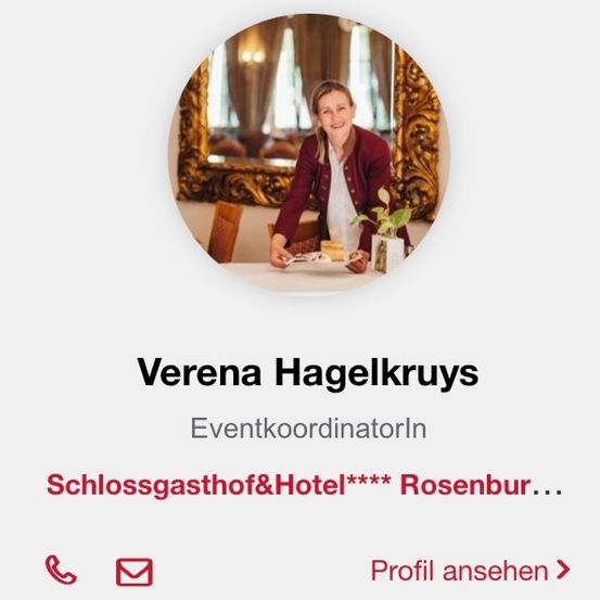 Ein Foto einer lächelnden Frau, Verena Hagelkruys, die in einem Restaurant vor einem Tisch steht. Sie hält einen Teller mit einem Sandwich. Dahinter befindet sich ein Spiegel mit goldenem Ornamentrahmen.