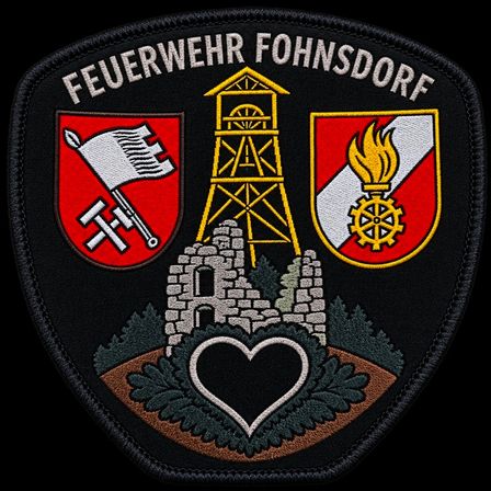 Ein Feuerwehrabzeichen mit dem Namen 'Feuerwehr Fohnsdorf' oben, mit einem Turm, einem Herz und zwei Wappen auf beiden Seiten. Der Hintergrund ist schwarz.